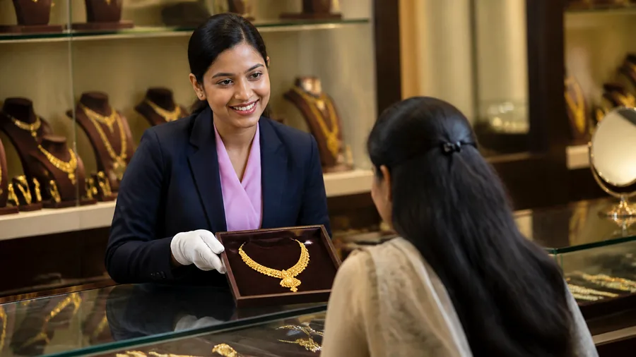 A jewellery showroom associate in gloves showing a gold necklace to a customer across the counter