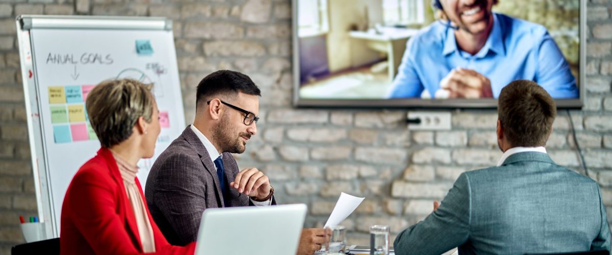 Group of entrepreneurs having a business meeting and communicating with their colleague via video call in the office.